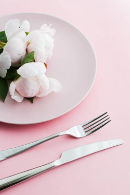 Pembe arka planda şakayık çiçekli yemek tabağı ve çatal bıçak seti. Etkinlik dekorasyonu ve menü markalaşması için en üst masa takımı.
