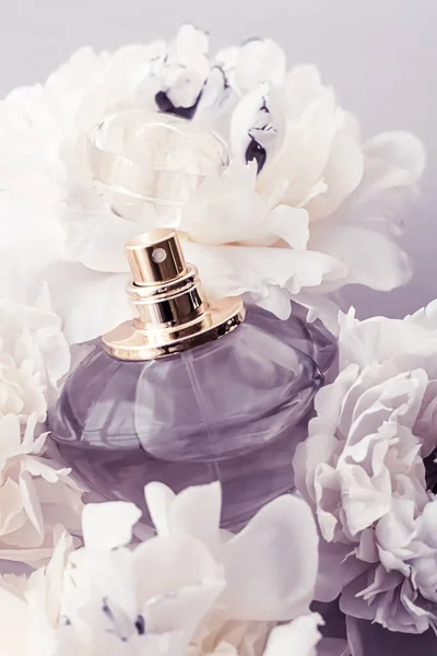 Фиолетовый флакон аромата в качестве роскошного парфюмерного продукта на фоне пионских цветов, парфюмерной рекламы и брендинга красоты — стоковое фото