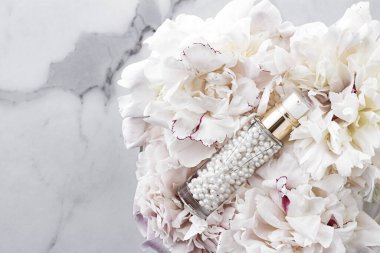 Çiçeklerin arka planında yaşlanma karşıtı cilt ürünü olarak lüks kozmetik şişesi, vücut bakımı için boş etiket ambalajı