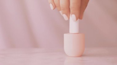 Pembe güzellik ürünü sahnesi, Fransız manikürü için kadın eli ve tırnak cilası şişeleri mermer masa üzerindeki renkli pastel oje, makyaj ve kozmetik marka.