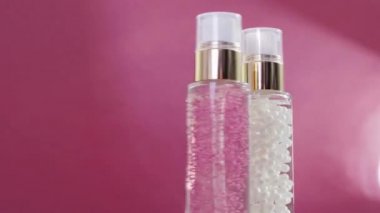 Şatafatlı cilt bakım ürünleri ve pembe arka planda parlak ışık parlamaları, makyaj malzemesi ve cilt bakımı rutini olarak serum jeli.