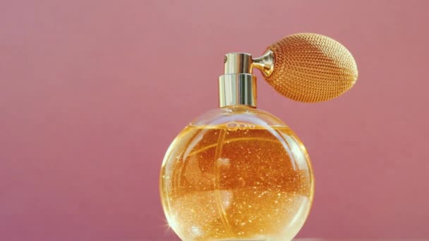 Frasco de perfume dorado de lujo y destellos de luz brillante sobre fondo rosa, aroma de fragancia glamorosa como producto de perfumería para la marca de cosméticos y belleza — Vídeos de Stock