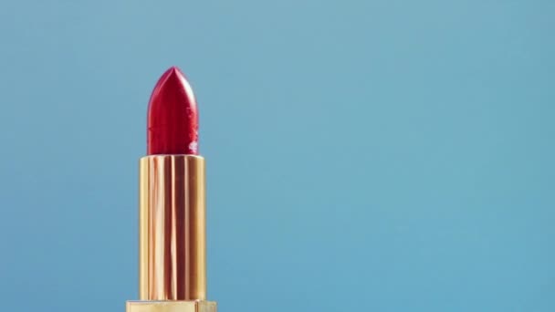 Schicker roter Lippenstift in goldener Röhre auf blauem Hintergrund und leuchtenden Lichterketten, Luxus-Make-up-Produkt und Urlaubskosmetik für Beauty-Marken — Stockvideo