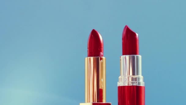 Две шикарные красные помады на синем фоне и яркие световые вспышки, роскошный косметический продукт и праздничная косметика для бренда красоты — стоковое видео