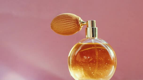 Frasco de perfume dorado de lujo y destellos de luz brillante sobre fondo rosa, aroma de fragancia glamorosa como producto de perfumería para la marca de cosméticos y belleza — Vídeos de Stock