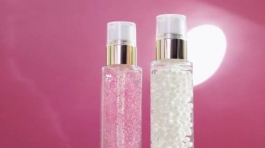 Şatafatlı cilt bakım ürünleri ve pembe arka planda parlak ışık parlamaları, makyaj malzemesi ve cilt bakımı rutini olarak serum jeli.
