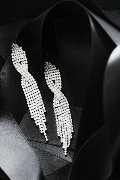 Luxury diamond earrings on black silk ribbon as background, jewelry and fashion brand