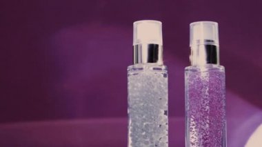 Makyaj malzemesi ve serum jeli lüks cilt ürünleri ve mor arka planda parlak ışık parlamaları, yüz estetiği ve güzellik markası için cilt bakımı rutini