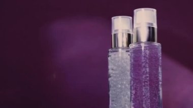 Makyaj malzemesi ve serum jeli lüks cilt ürünleri ve mor arka planda parlak ışık parlamaları, yüz estetiği ve güzellik markası için cilt bakımı rutini