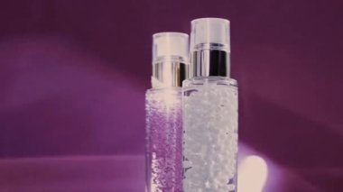 Makyaj malzemesi ve serum jeli lüks cilt ürünleri ve mor arka planda parlak ışık parlamaları, yüz estetiği ve güzellik markası için cilt bakımı rutini