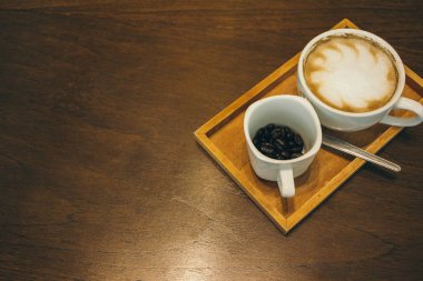 Kafede ahşap masada kahve bardağı ve kahve çekirdekleri