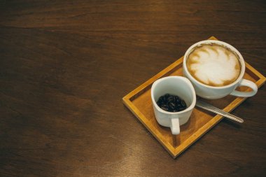 Kafede ahşap masada kahve bardağı ve kahve çekirdekleri