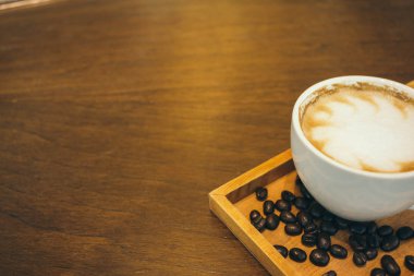 Kafede ahşap masada kahve bardağı ve kahve çekirdekleri