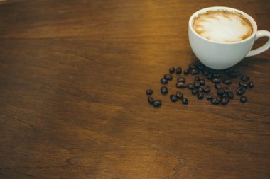 Kafede ahşap masada kahve bardağı ve kahve çekirdekleri