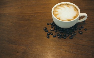 Kafede ahşap masada kahve bardağı ve kahve çekirdekleri