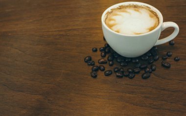 Kafede ahşap masada kahve bardağı ve kahve çekirdekleri