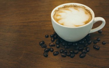 Kafede ahşap masada kahve bardağı ve kahve çekirdekleri