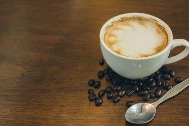 Kafede ahşap masada kahve bardağı ve kahve çekirdekleri