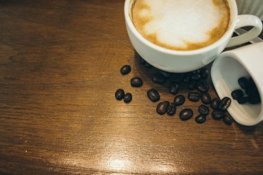 Kafede ahşap masada kahve bardağı ve kahve çekirdekleri