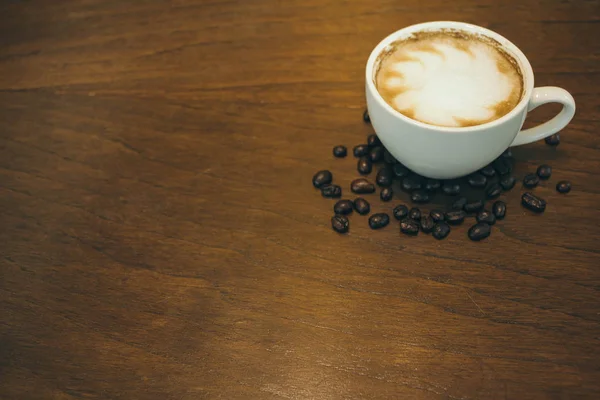 Kafede ahşap masada kahve bardağı ve kahve çekirdekleri