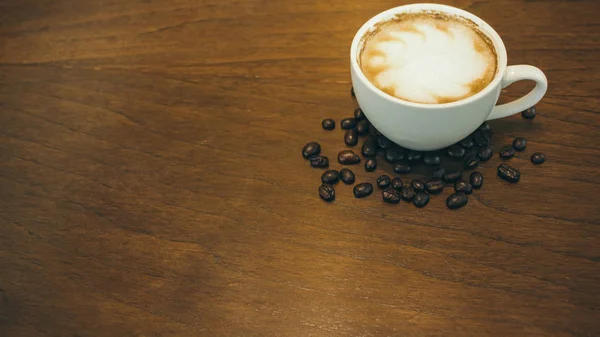 Kafede ahşap masada kahve bardağı ve kahve çekirdekleri