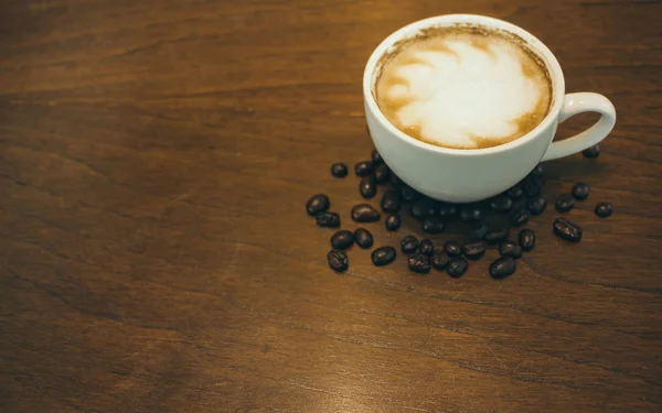 Kafede ahşap masada kahve bardağı ve kahve çekirdekleri