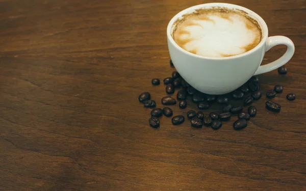 Kafede ahşap masada kahve bardağı ve kahve çekirdekleri
