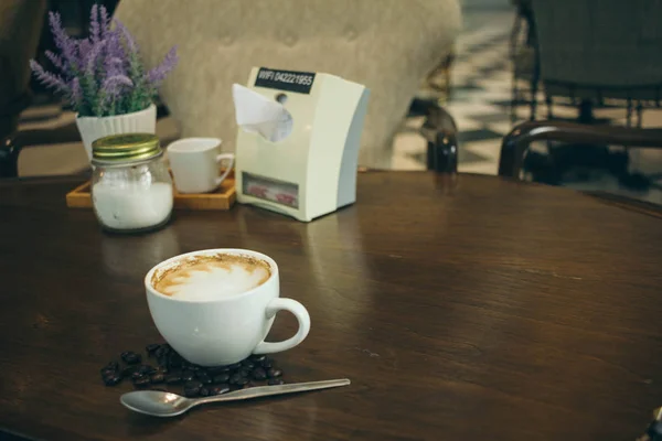Taza de café y granos de café en la mesa de madera en la cafetería — Foto de Stock