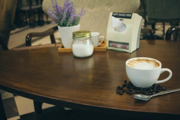 Taza de café y granos de café en la mesa de madera en la cafetería — Foto de Stock