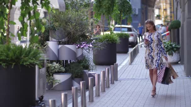 Kvinna med en shopping påsar promenader i en stad efter shopping dag vid solnedgången — Stockvideo
