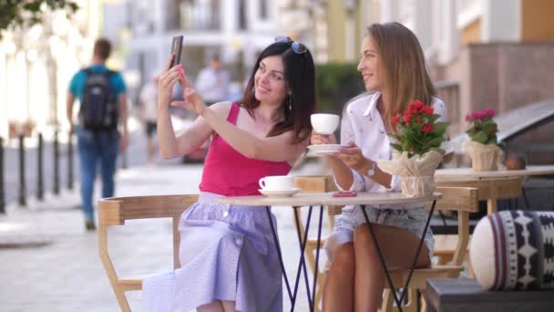 Due belle giovani donne si siedono a un tavolo in un caffè e si fanno un selfie al telefono 4k slow motion — Video Stock