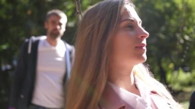 salıncakta sürme ve rahatlatıcı güzel genç anne. Arka planda onun ailesidir. Parkta. 4 k. ağır çekim.