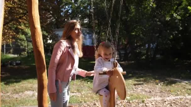 Όμορφη νεαρή ευτυχισμένη μητέρα εναλλαγές της κόρης του σε ένα πάρκο σε μια κούνια. 4 k. αργή κίνηση. — Αρχείο Βίντεο
