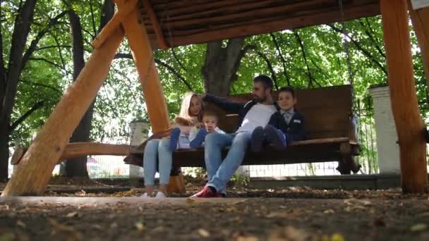 Gelukkig jonge gezin vader, moeder, zoon en dochtertje rijden op een schommel in het park. Lachen en glimlachen. 4 k. Slowmotion — Stockvideo