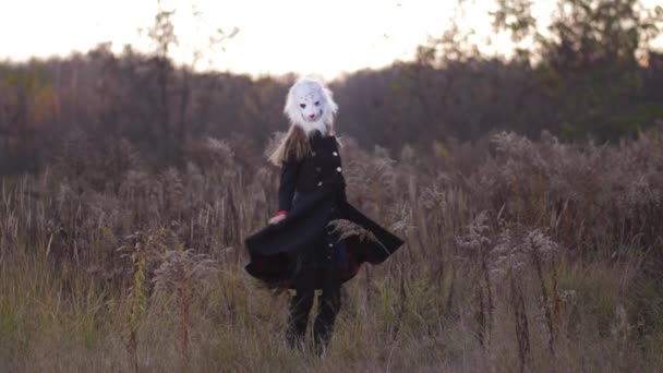 Plan general. En el campo de otoño, una chica bailando con una máscara de oso. La mujer está vestida con abrigos azules 4K Slow Mo — Vídeos de Stock