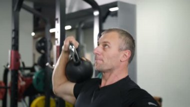 Yakın çekim. Yakışıklı adam ile bir kettlebell 4 k spor salonunda egzersiz yaparak yavaş Mo