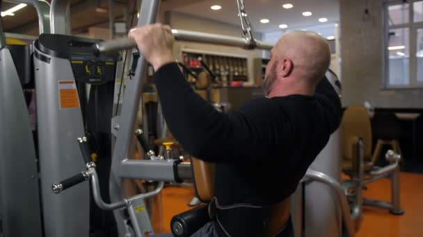 A man with a beautiful body, doing an exercise on the simulator, aimed at the back muscles. View from the back 4K Slow Mo — Stock Video