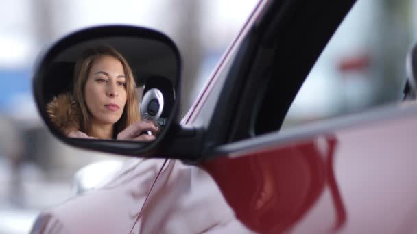 Hermosa chica en el coche se pinta los labios con lápiz labial rosa, mira a la cámara a través del reflejo en el espejo lateral y sonríe 4K Lento Mo — Vídeos de Stock