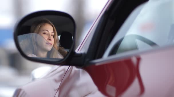 Όμορφο κορίτσι χαμηλώνει το παράθυρο στο αυτοκίνητο, κοιτάζει στον καθρέφτη πλευρά, κύματα το χέρι της και χαμογελάει 4k αργή Mo — Αρχείο Βίντεο