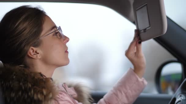 Cose-up. Chica en el coche, se mira en el espejo superior, endereza su cabello 4K Lento Mo — Vídeo de stock