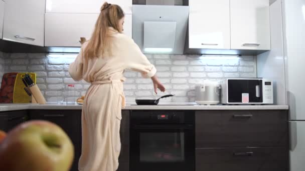 穿着浴衣的美丽女孩 在厨房里用勺子和煎锅跳舞唱歌 — 图库视频影像