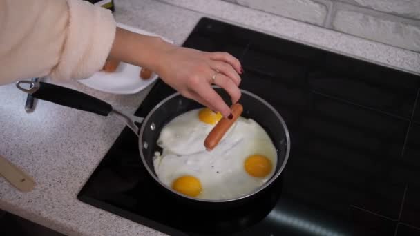 Œufs brouillés dans une poêle, la fille y ajoute des saucisses .