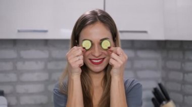 Bir kızın yakın çekim. O iki salatalık dilim gözleri önünde tutan, onları kaldırır ve farklı yüz ifadeleri yapar. 4 k yavaş Mo