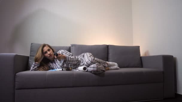 Больная девочка лежит дома на диване. Перед планшетом она смотрит телевизор, отдыхает. 4K Slow Mo — стоковое видео