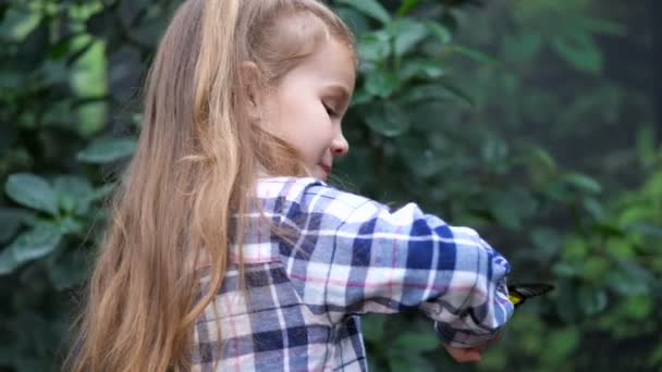 A beautiful girl is standing with her back, turning, there is a butterfly on her hand. The girl looks into the frame and smiles. 4K Slow Mo — Stock Video