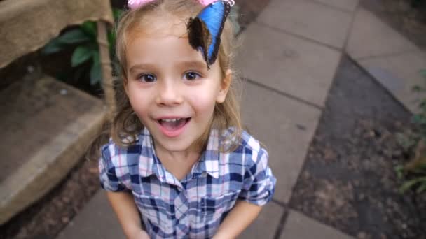 A menina está muito feliz e sorrindo, porque uma linda borboleta pousou em sua cabeça. 4K Mo lento — Vídeo de Stock