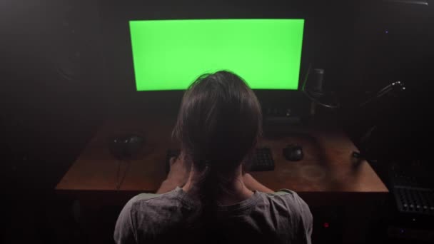 Um homem com cabelo comprido imprime texto no teclado, tem uma tela verde no monitor. 4K Mo lento — Vídeo de Stock