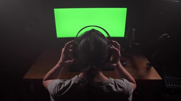 Um homem em fones de ouvido olha para a tela verde do monitor, remove os fones de ouvido, olha para a tela, começa a digitar. 4K Mo lento — Vídeo de Stock