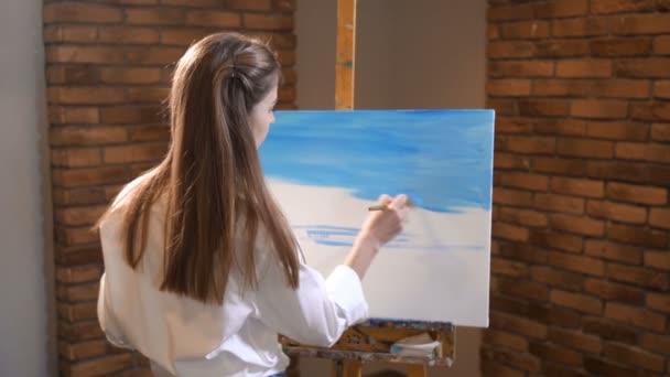 Hübsche Frau fokussiert malt ein Bild. Sie füllt die Leinwand mit blauer Farbe. 4k langsam mo — Stockvideo