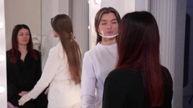 Güzellik uzmanı aynanın önünde sandalyede oturan kıza bakar, uzman hastayı değerlendirir. 4k Yavaş Mo